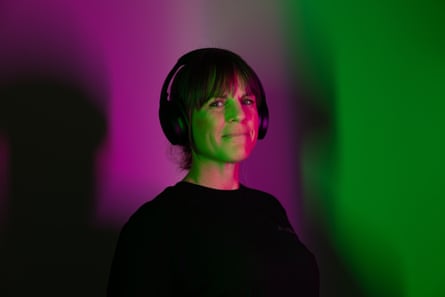 A woman wearing headphones against a background of ombre purple and green light.