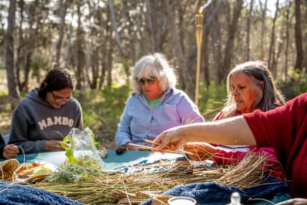 Three women weave with reeds and grasses outdoors on Kumarangk, South Australia