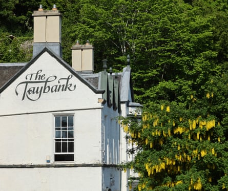 Exterior shot on a sunny day of the white walls of the Taybank, next to a tree with yellow flowers