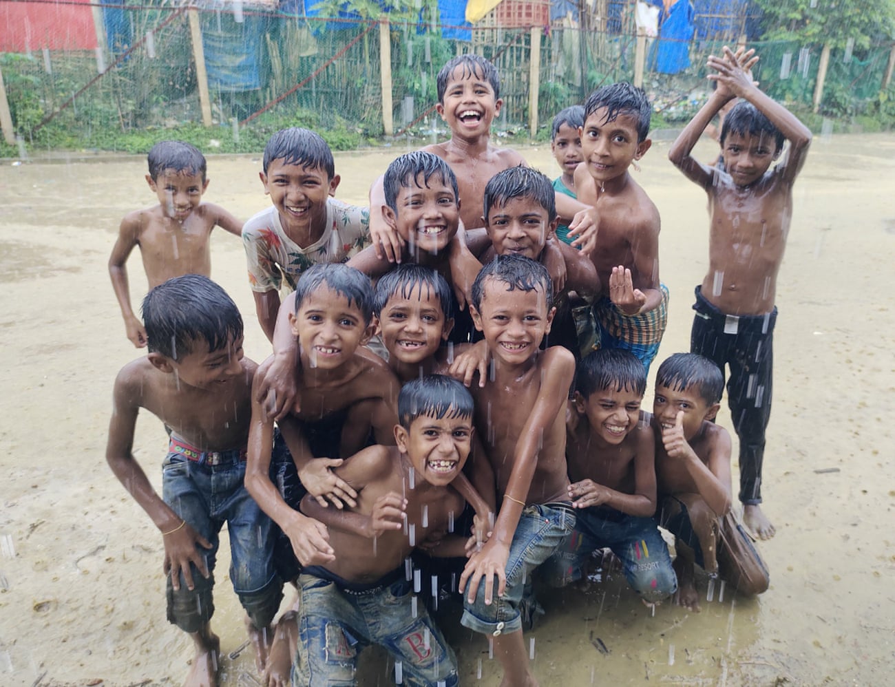 A group of Rohingya children play in the rain as water flows outside their shelters in refugee camps in Cox's Bazar, Bangladesh.