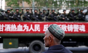 A Uighur man looks on at a truck carrying paramilitary police officers in Urumqi, Xinjiang.