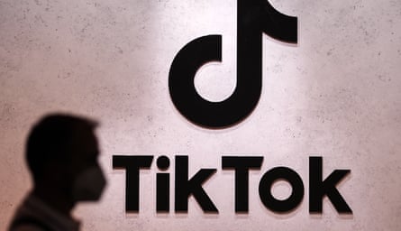 A person’s silhouette can be seen on a wall with the TikTok music note logo.