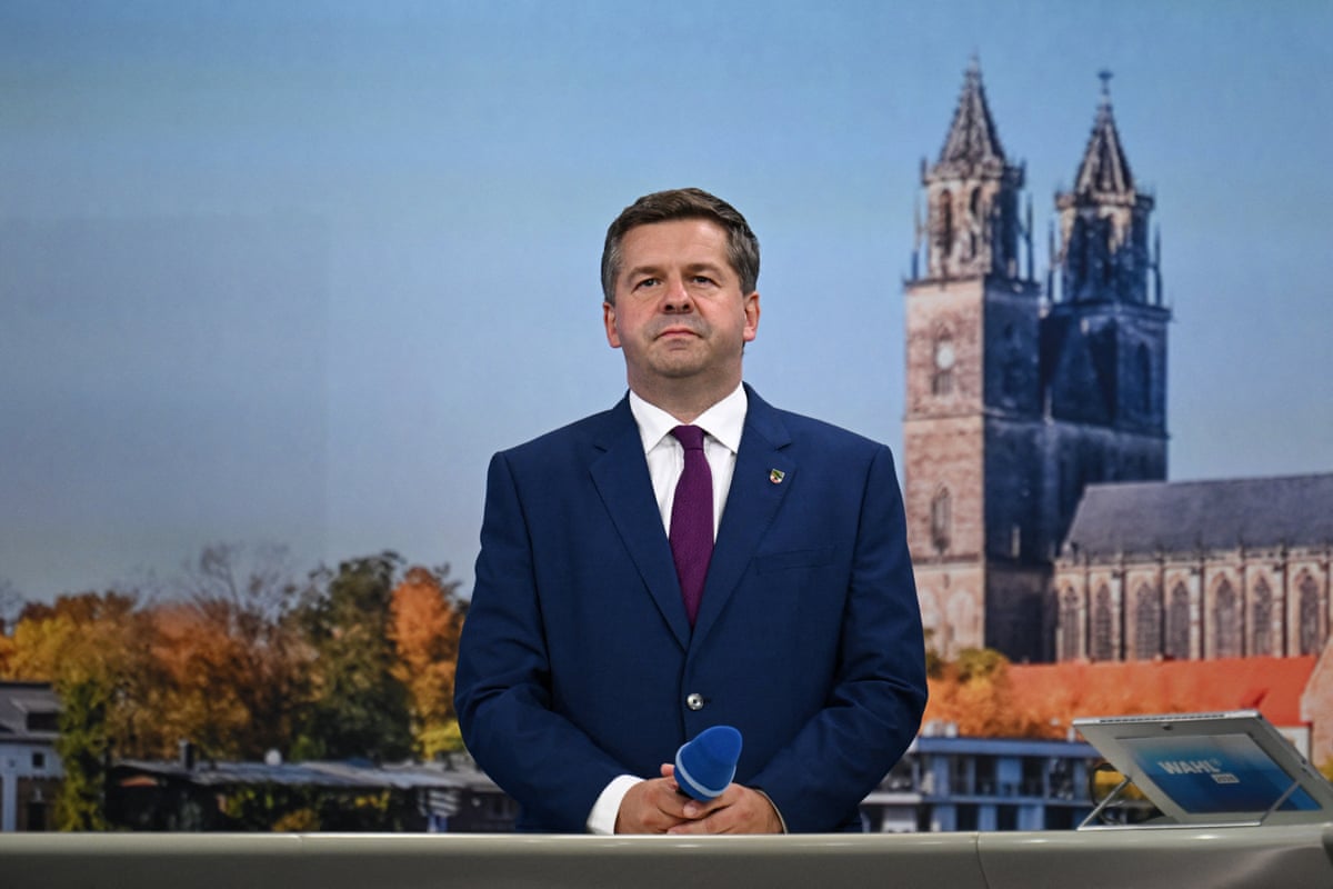 Sven Schulze stands holding a microphone in front of a backdrop depicting a tall church or cathedral.