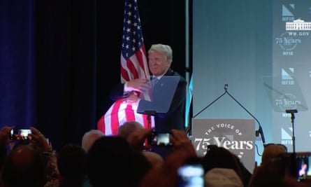 Donald Trump hugs the US flag after his speech to NFIB conference.