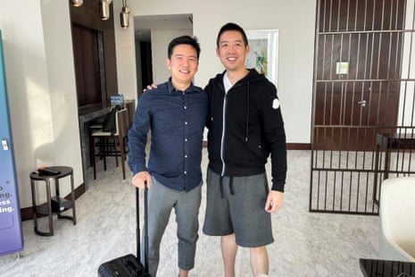 two men pose for picture, one with a suitcase