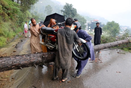 People get across a fallen tree in Pakistani-administered Kashmir after flash floods and landslides struck northern Pakistan.