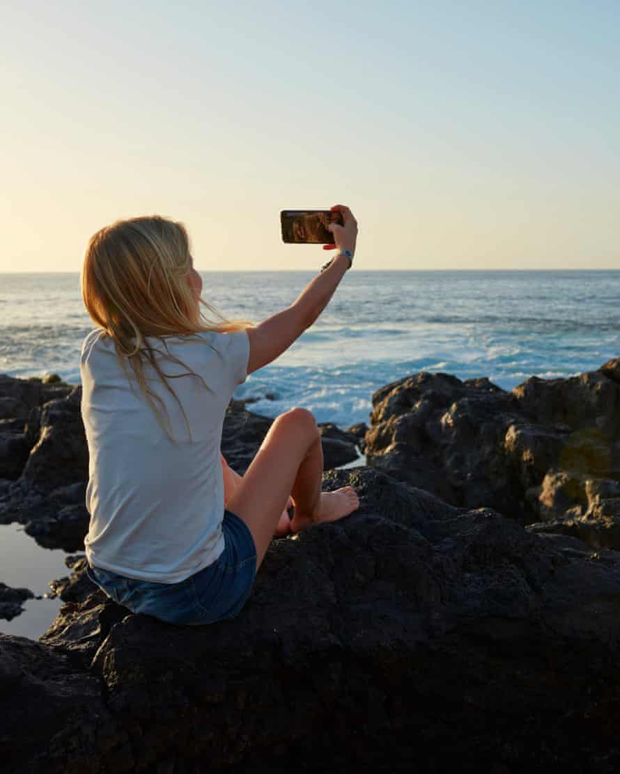 Girl taking selfie by the sea at sunset.