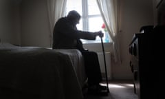An older man sitting on the edge of a bed holding a cane