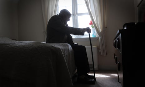 An older man sitting on the edge of a bed holding a walking stick