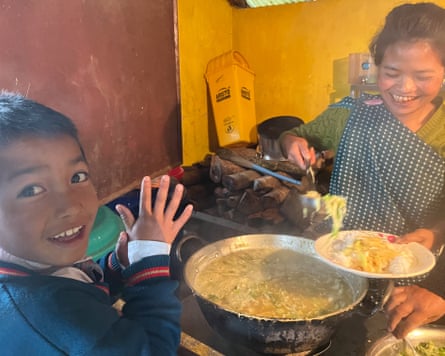 A smiling woman puts food on a plate while a boy smiles at the camera