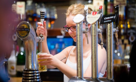 A young woman pulls a pint of lager in a bar.