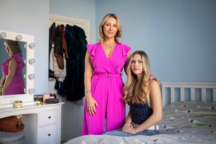 Sophie Blake and her daughter at home in Brighton. Sophie is wearing a hot-pink jumpsuit standing next to Maya who is seated on a bed.