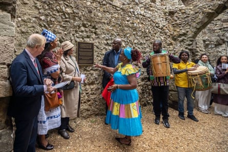 A Garifuna woman gestures near a new memorial plaque at Portchester Castle, surrounded by onlookers and drummers
