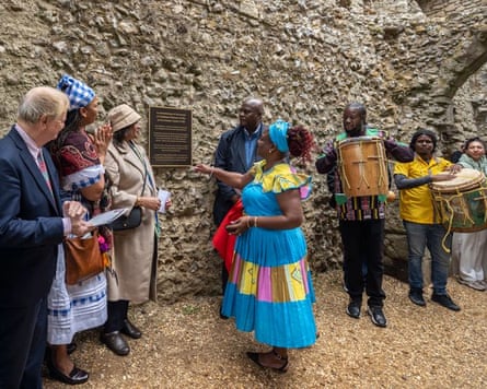 A Garifuna woman gestures near a new memorial plaque at Portchester Castle, surrounded by onlookers and drummers