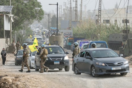 Uniformed men patrol near a queue of cars.