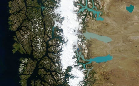 Aerial view of a snow-capped mountain range with glacial lakes seen on the interior side and fissures created by water channels descending to the sea on the other