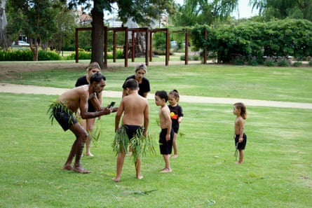 An Aboriginal man is talking to some children on the grass as they prepare to perform a dance