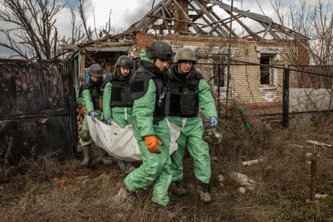 The corpse of a Russian soldier is carried from a destroyed building by Ukrainian volunteers in a deserted village in Donetsk