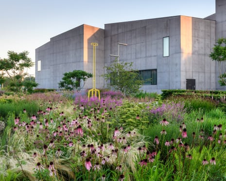 A wildflower garden with a big yellow metal sculpture of a fork in front of a modernist concrete building.
