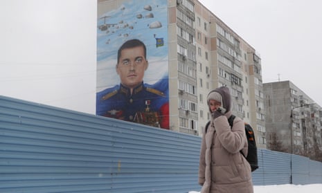 A woman walks next to a mural on a wall of an apartment block by Russian artist Ilya Demchinko, with a portrait of Russian soldier Alexey Osokin.