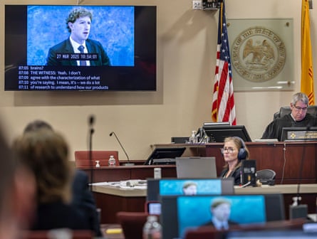 TV plays video of man in suit as people sit at tables in courtroom
