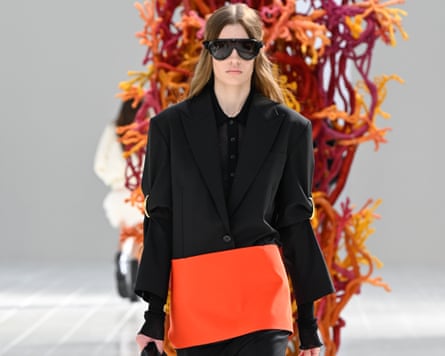 A model wears a black suit with a bold slash of tangerine at the jacket hem