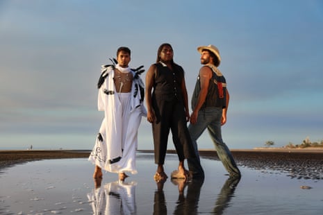 Three figures stand on a beach