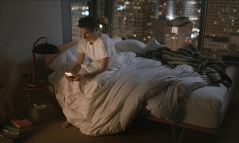 Man wearing white T-shirt sits on bed holding phone
