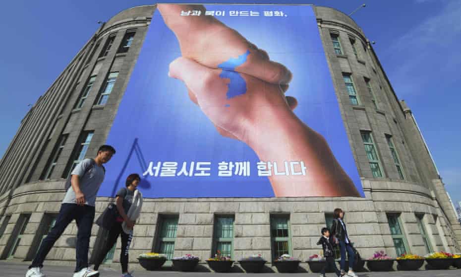 Pedestrians walk past a banner showing two hands forming the shape of the Korean peninsula, to support the upcoming inter-Korean summit in Seoul.