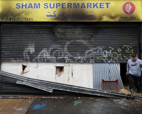 A man emerges from a gap in the charred and broken shutters of shop with Arabic script on its sign