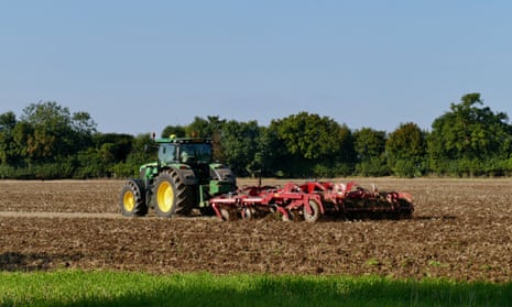 A green tractor pulls a plough in a field