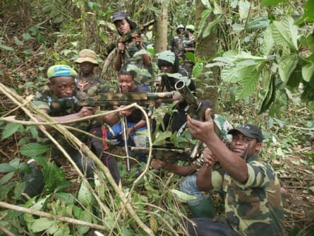 An undated photo showing a group of men in camouflage clothes, with one pointing a rifle towards the sky from behind some bushes