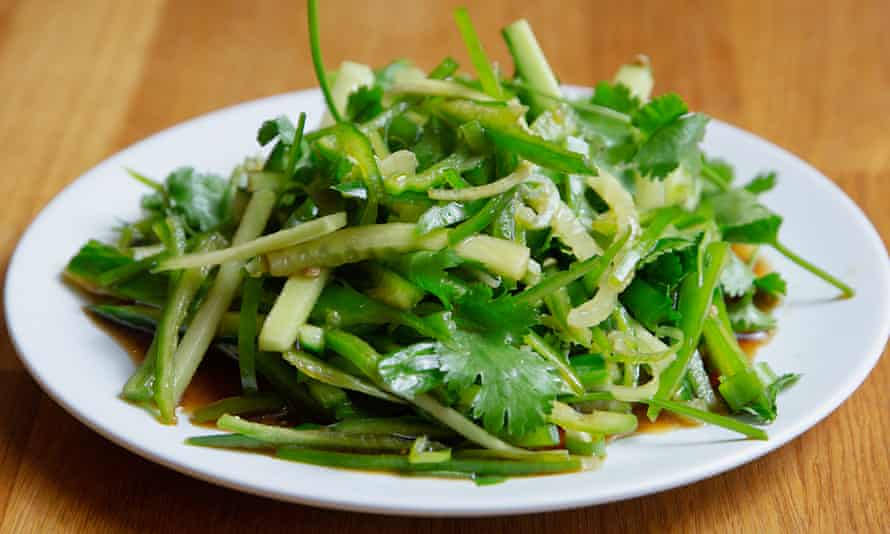 A bright green pile of cilantro, julienned cucumber and spring onions on a round white plate