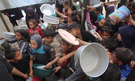 A throng of people, many of them children, holding up food bowls in a queue