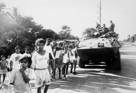 black and white image of a dozen children alongside a tank on a road