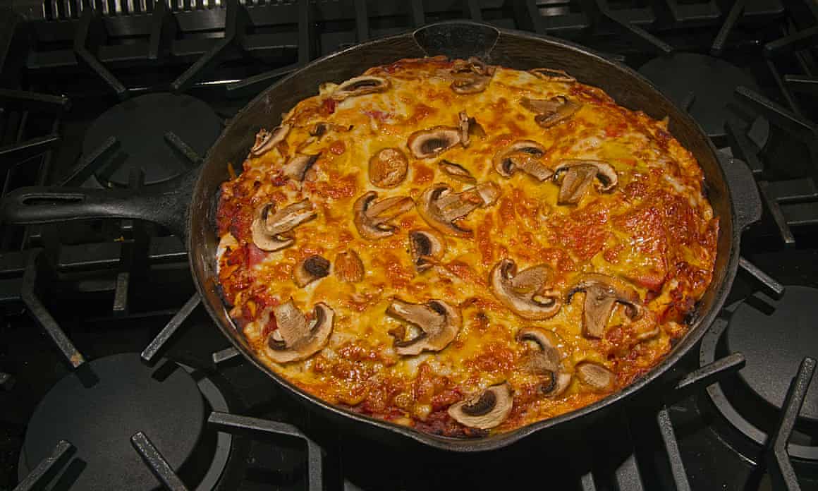 A well-cooked mushroom frittata in a dark pan on a gas stove
