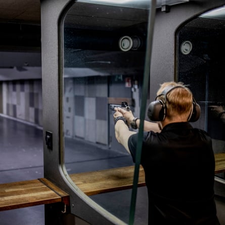 A man wearing ear defenders aims a gun at a target at an underground shooting range under Helsinki.