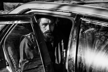 A man sitting in a car with the door open, holding a gun