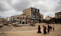 Palestinians walk past damaged buildings in Khan Yunis