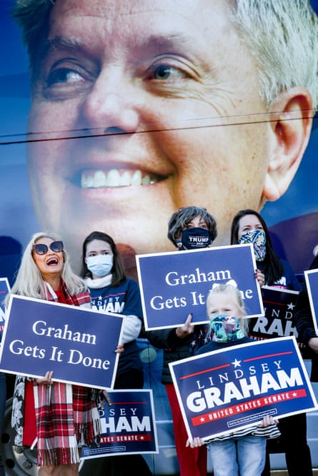 People hold Lindsey Graham campaign signs with a large photo of him as a backdrop.