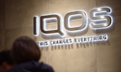 A person passing an illuminated sign on a wall reading: 'IQOS - This changes everything'