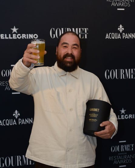 A man in a white button shirt raises a glass of beer while holding his award for ‘best new talent’