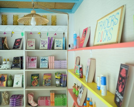 A corner decorated in the style of a beach hut with books displayed on shelves on the walls, interspersed with suncream, chapstick and a sign that says ‘Traders dicks’