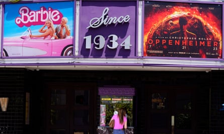 A person buying a movie ticket underneath a marquee featuring the films Barbie and Oppenheimer.