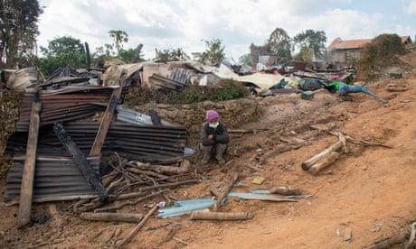 A man sits in front of a house that was burned by a military air strike