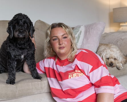 A woman in a pink and red jumper and a black dog and a white dog either side of her on a white sofa