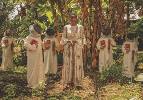An African woman with her hands chained stands in a forest surrounded by figures draped in white with basins on their head and holding Bibles