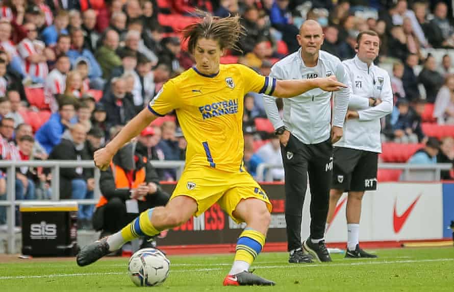 AFC Wimbledon head coach Mark Robinson leans forward as Alex Woodyard plays a pass to Sunderland.