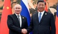 Vladimir Putin and Xi Jinping shake hands while smiling