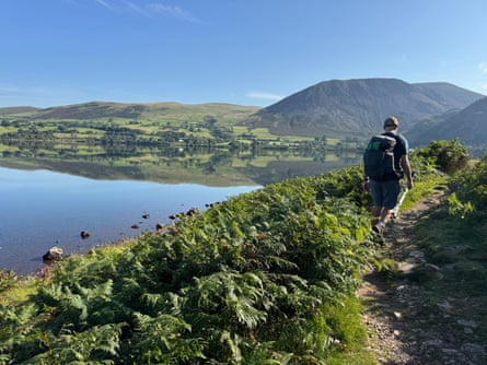 Man walking near lake on a summer's day, with the Lake District scenery reflected in it